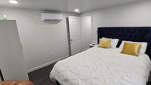 Une chambre à coucher comprenant un lit, des tables de chevet, une armoire, une porte et un appareil de climatisation.