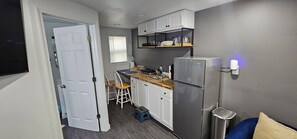 A compact kitchen with white cabinets, a stainless steel refrigerator, and a wooden countertop.