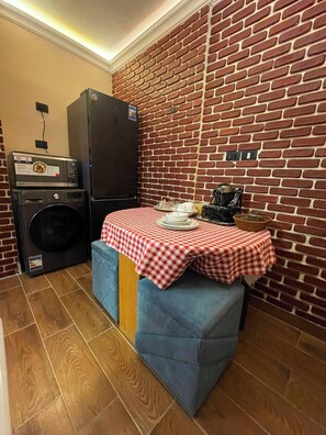 Cozinha compacta com parede de tijolos, máquina de lavar, frigorífico e mesa com toalha de mesa xadrez.