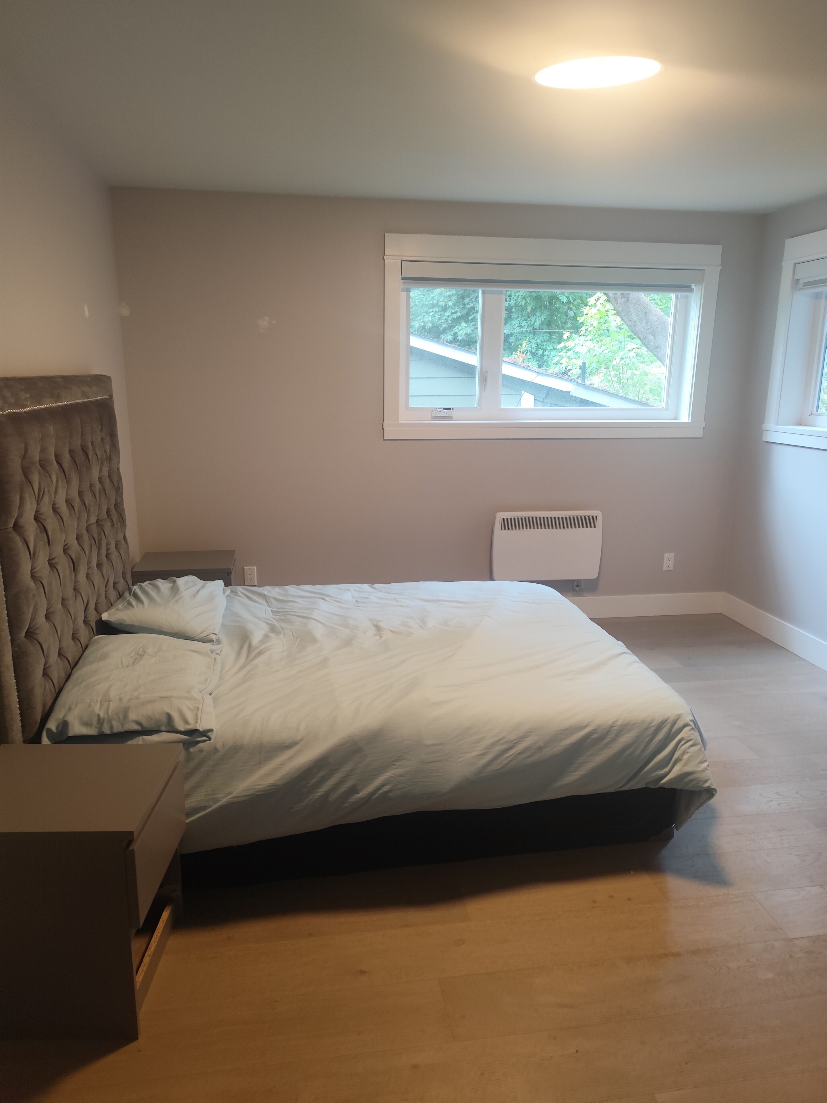 A bedroom with a bed, a headboard, a window, and a radiator.