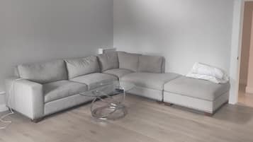 Ein modernes Wohnzimmer mit einem Ecksofa, einem Glastisch und einer modernen Deckenleuchte.