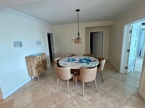 Een eetgedeelte met een ronde tafel, stoelen, een hanglamp en een houten servieskast.