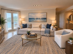 Ein Wohnzimmer mit Sofa, Sesseln und Couchtisch, einem Gemälde über dem Sofa sowie Blick durch eine Glastür.