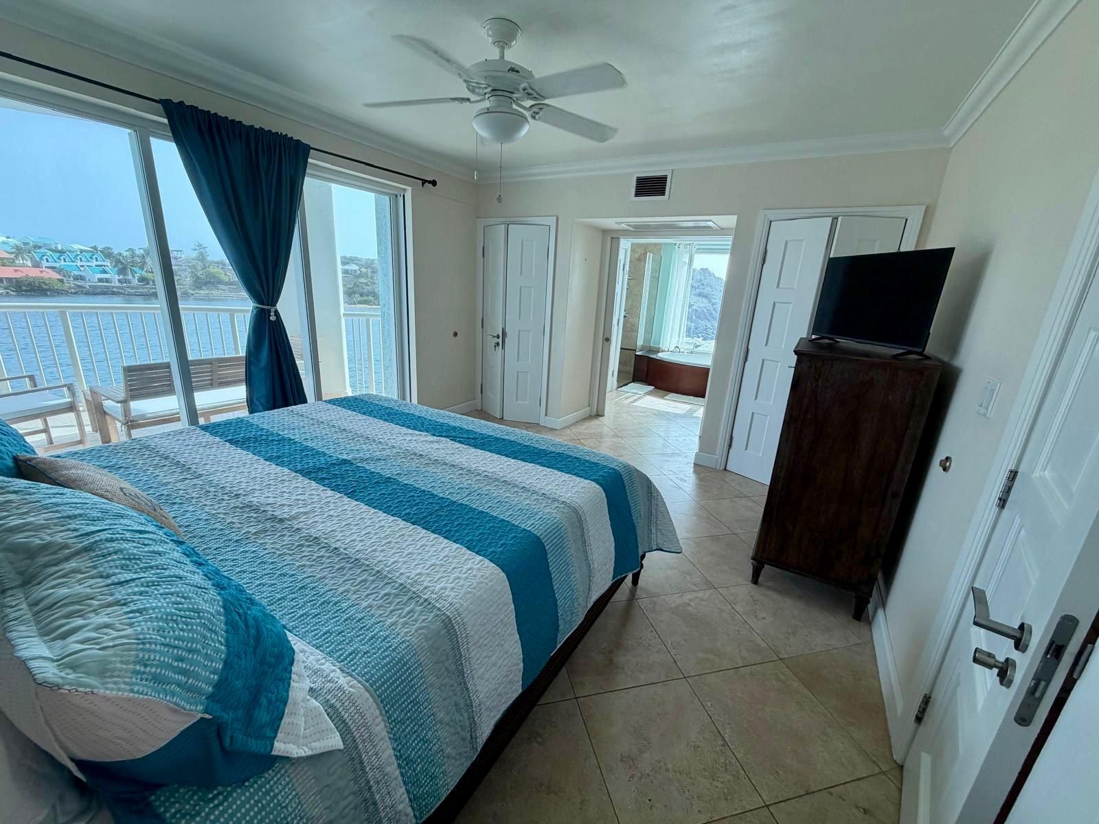 A hotel room with a bed, a television on a cabinet, and a view of the sea through large windows.