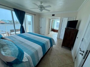A hotel room with a bed, a television on a cabinet, and a view of the sea through large windows. - The Lighthouse, Unit 3A-Oyster Bay, St. Maarten. Walk to Beach (Oyster Bay)