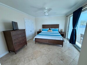 Ein Schlafzimmer mit einem Bett, einem Schminktisch, einem Deckenventilator und Blick durch ein Fenster.