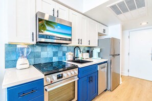 A modern kitchen with white cabinets, a built-in stove, a blender, and a refrigerator. - Oceanfront Blue Haven at Yachtsman by Skywheel! (Myrtle Beach)