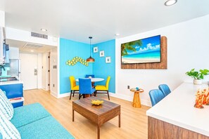 Ein modernes Wohnzimmer mit blauer Akzentwand, ein Essbereich mit gelben Stühlen und eine im Hintergrund sichtbare Küche.