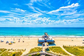 A beach with a pier, beach umbrellas, and a clear blue sky. - Oceanfront Blue Haven at Yachtsman by Skywheel! (Myrtle Beach)