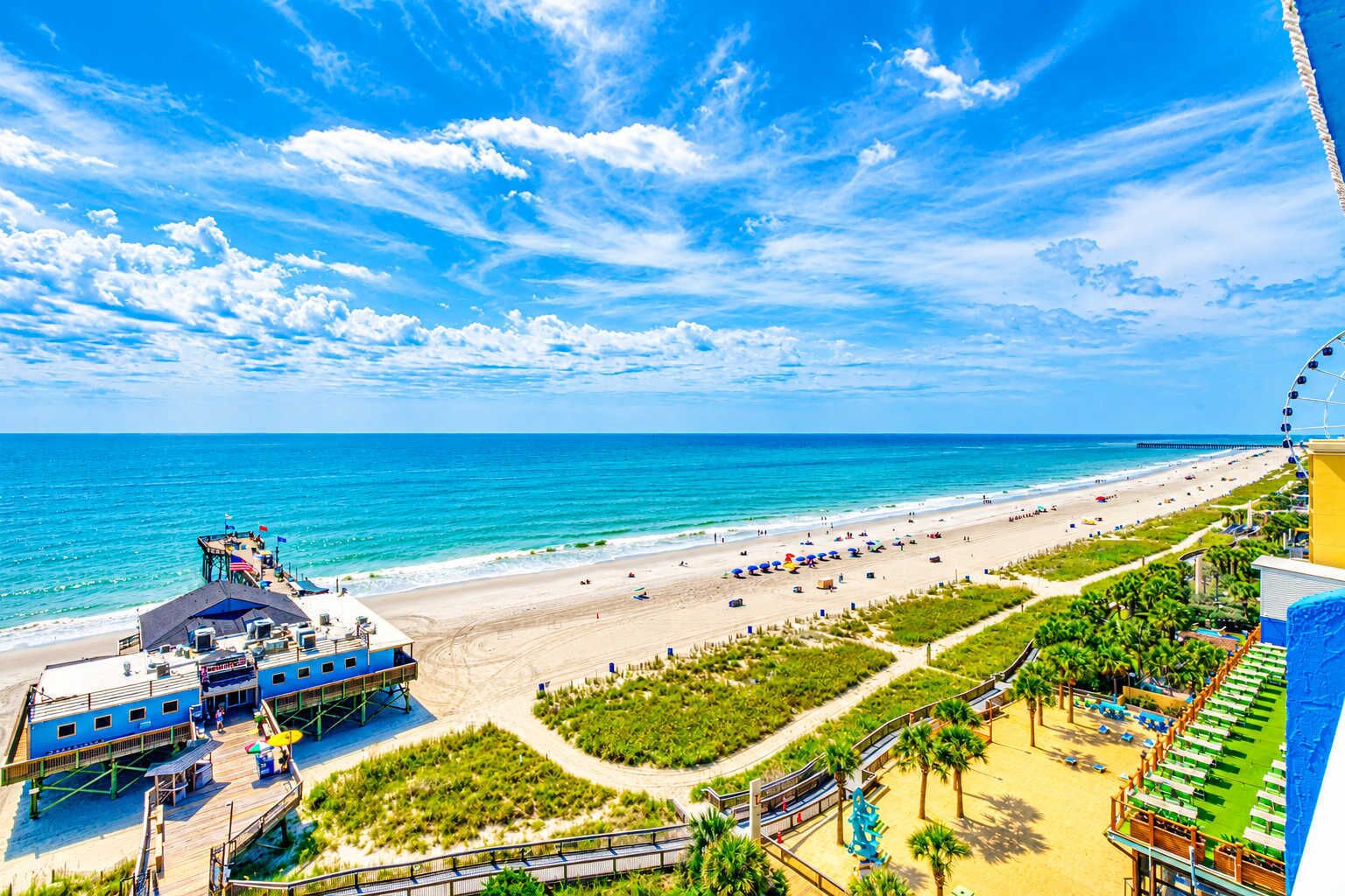 A beach resort with a pier, beach umbrellas, and a Ferris wheel.