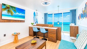 Ett modernt rum med ett skrivbord, stolar, ett matbord och utsikt över havet genom stora fönster.