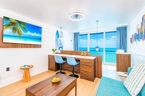 Ein modernes Zimmer mit Schreibtisch, Stühlen, einem Esstisch und Meerblick durch große Fenster.