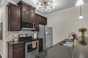 A kitchen with dark wood cabinets, stainless steel appliances, a granite countertop, and a modern light fixture. - Telluride:5 BR/5 BA Home-2 Minutes from A&M Campus (College Station)