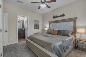 Une chambre à coucher comprenant un lit, un ventilateur de plafond, une table de chevet, une lampe, une commode et un miroir.