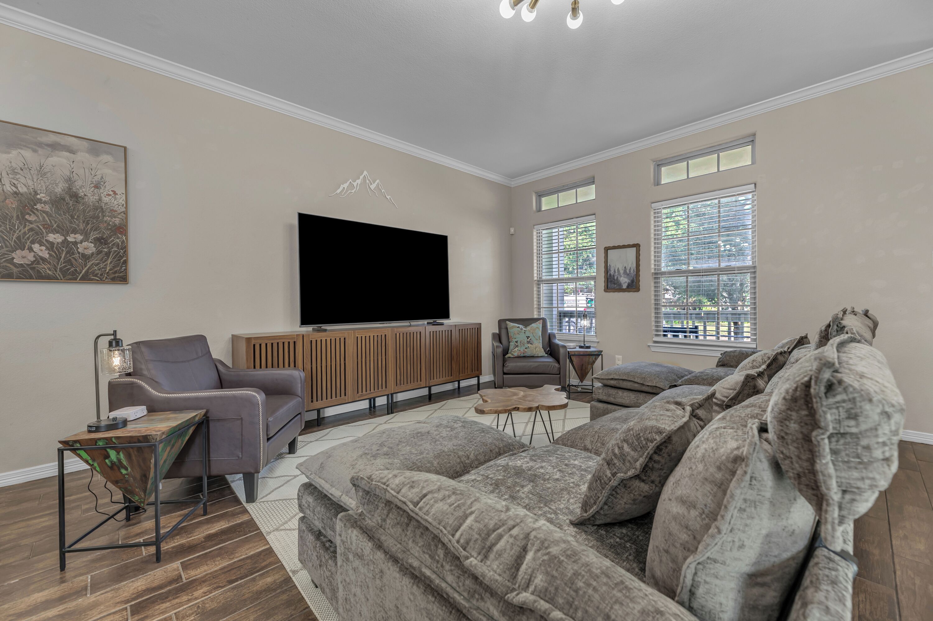 A modern living room with a large flat-screen TV, a sofa, a chair, and a coffee table.