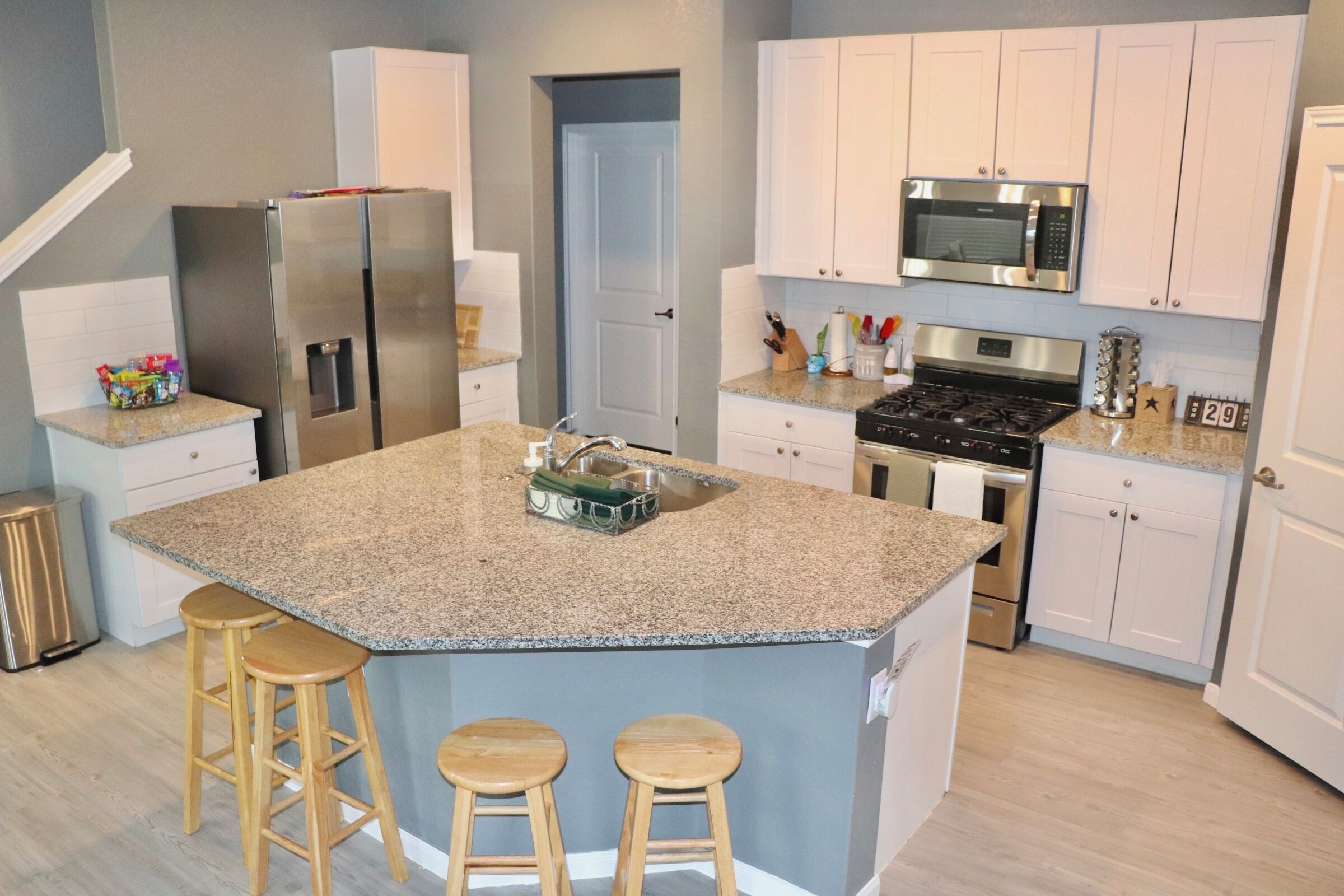 Una cocina moderna con encimeras de granito, electrodomésticos de acero inoxidable y una isla central con taburetes.