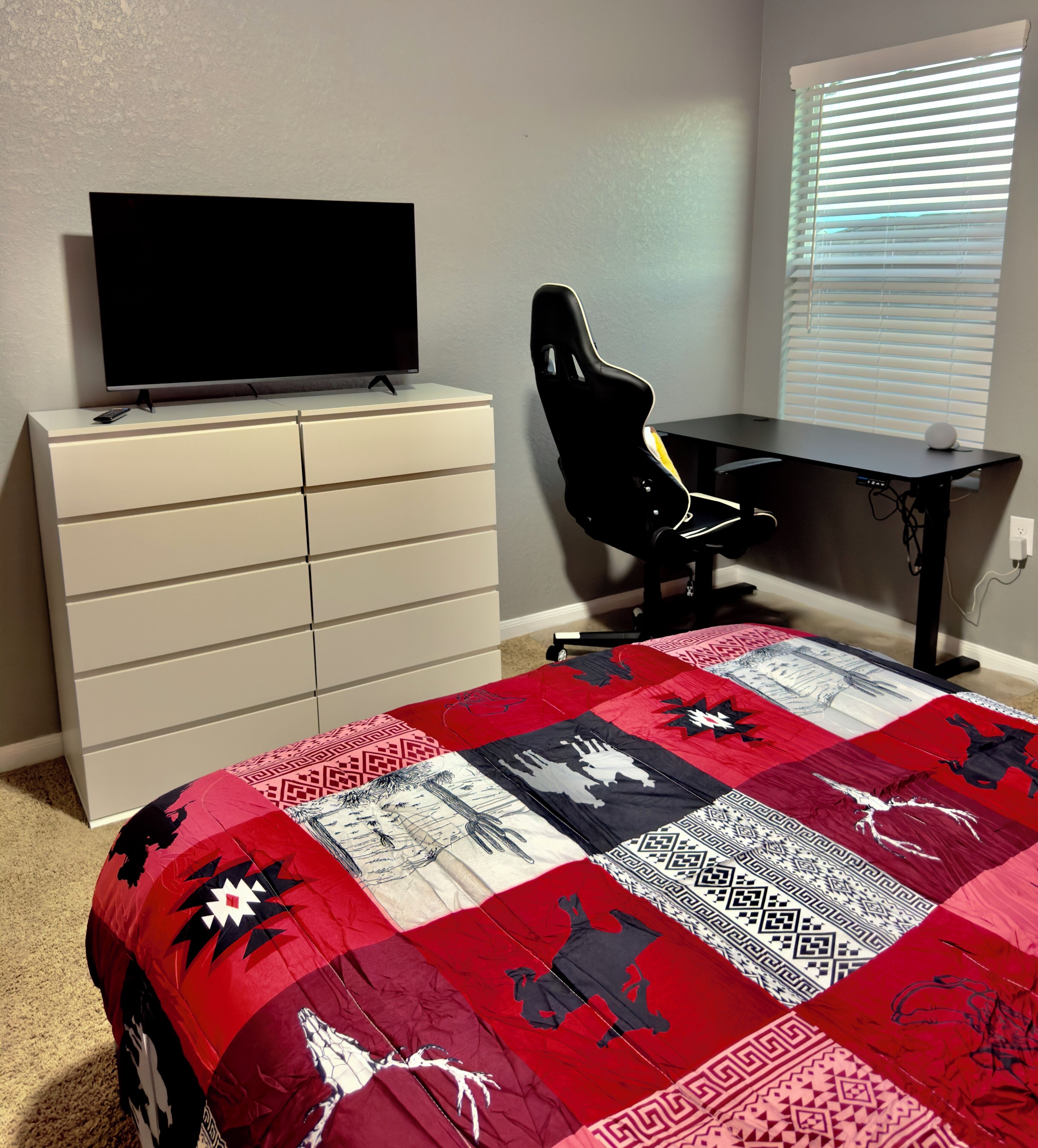 Un dormitorio con una cama, un televisor en un tocador, un escritorio y una silla.