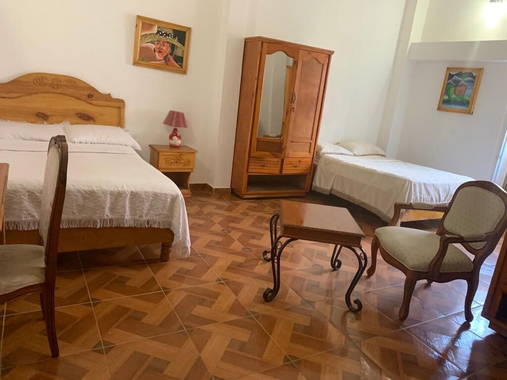 A bedroom with a wooden bed, a wooden wardrobe, a bedside table, a chair, and a small table.