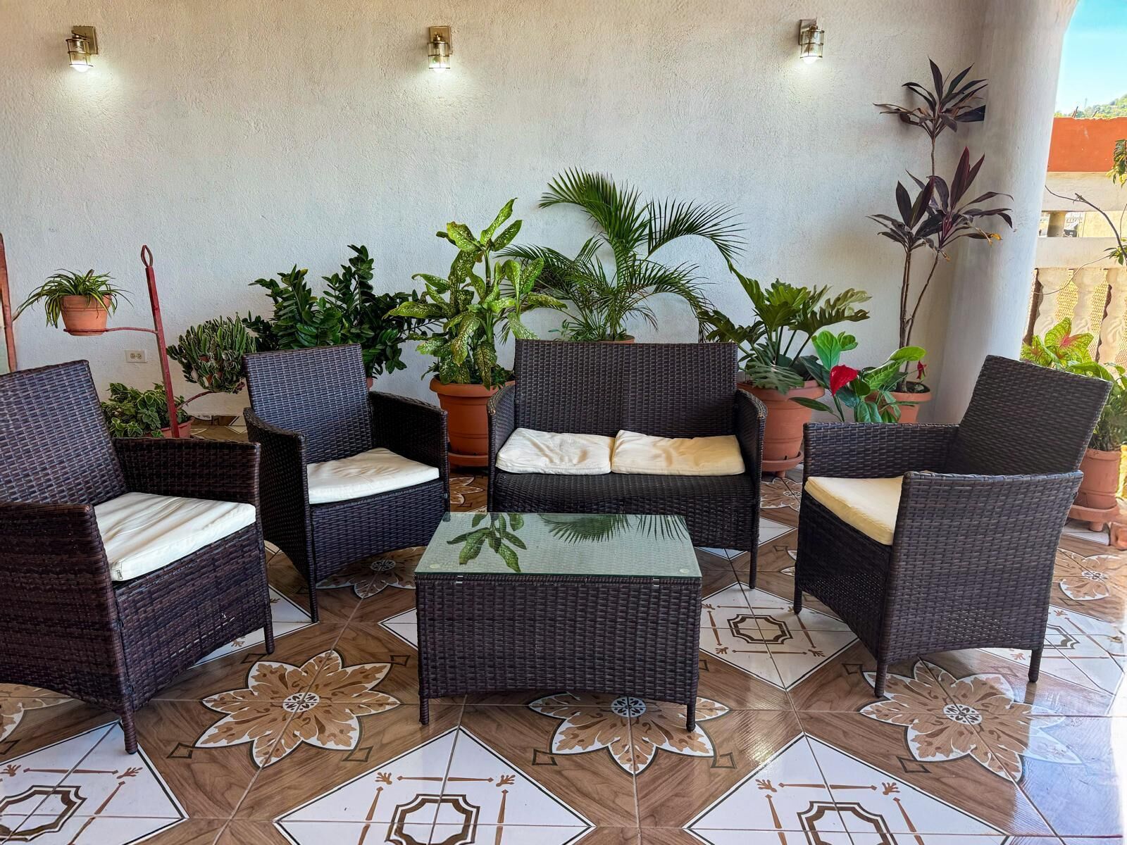 Uma área de pátio com móveis de vime, plantas em vasos e piso estampado.