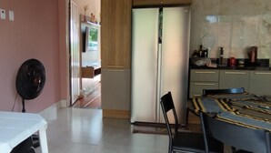 A room with a dining table, chairs, a fan, a refrigerator, and a kitchen area with cabinets and a countertop. - Cozy little house in Chapada dos Guimarães, 5 km from the Central Square. (Chapada dos Guimarães)