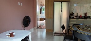 A room with a dining table, chairs, a fan, a refrigerator, and a kitchen area with cabinets and a countertop. - Cozy little house in Chapada dos Guimarães, 5 km from the Central Square. (Chapada dos Guimarães)