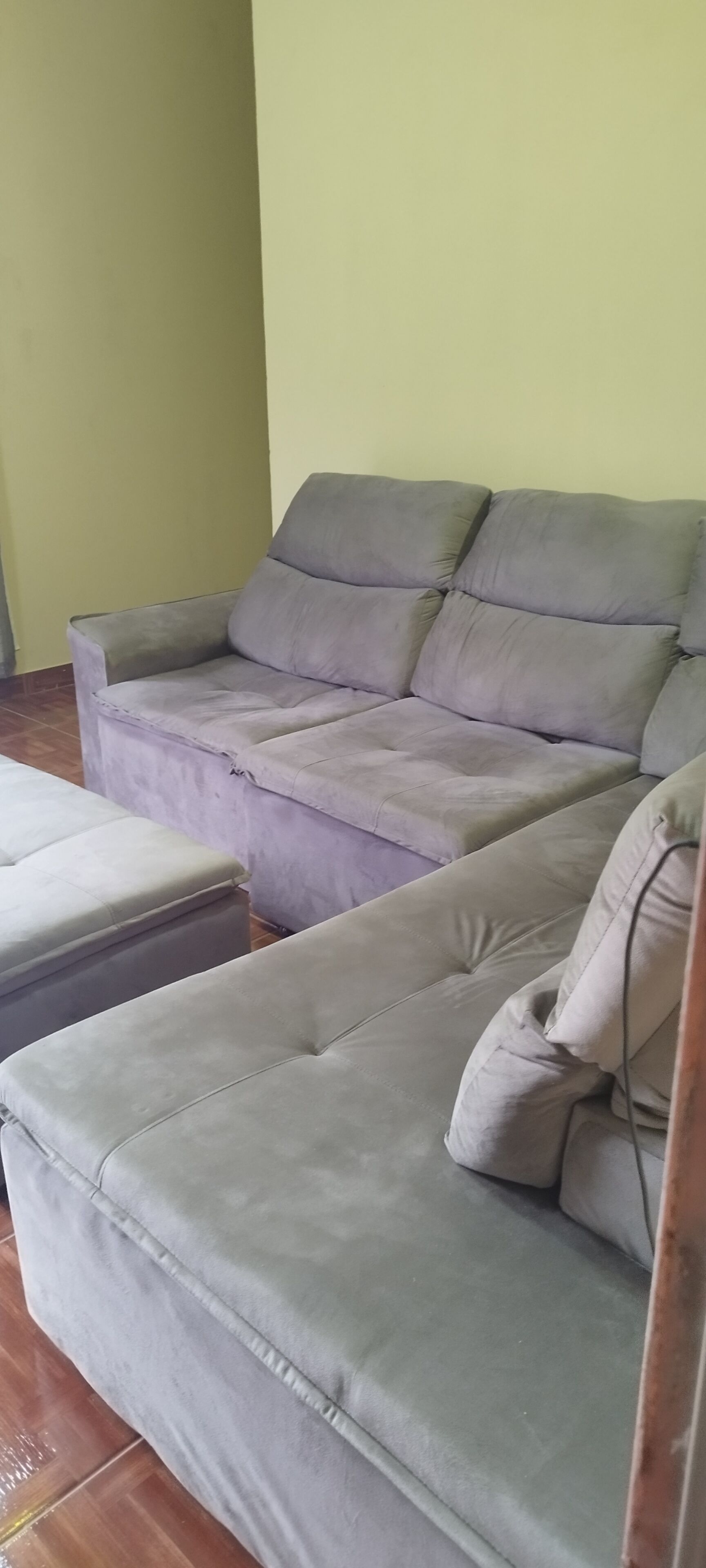 A grey sofa with a matching ottoman in a room with a tiled floor and a plain wall.