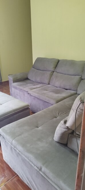 A grey sofa with a matching ottoman in a room with a tiled floor and a plain wall.