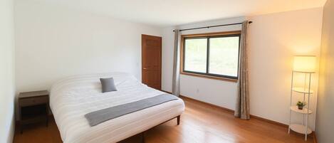 Un dormitorio con cama, mesita de noche, ventana con cortinas y lámpara de pie.