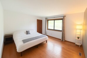 Un dormitorio con cama, mesita de noche, ventana con cortinas y lámpara de pie.
