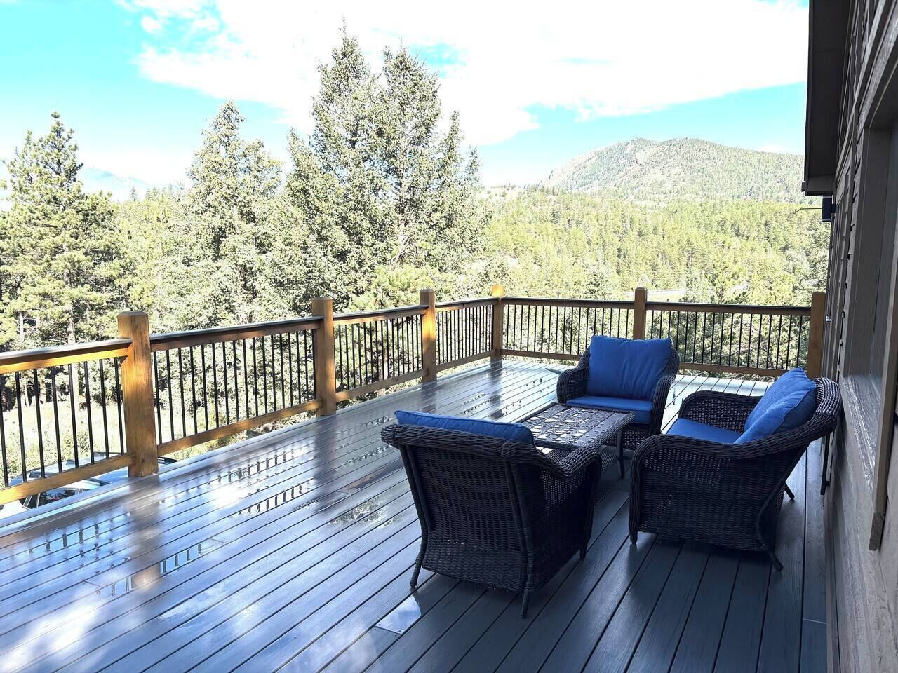 A wooden deck with wicker furniture and a railing overlooking a forested area.