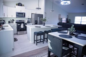 A modern kitchen with white cabinetry, stainless steel appliances, and a central island with bar stools. - Charming  brand new 3-bedroom house in Ocala with cool AC breeze (Ocala)