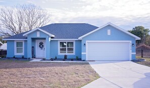 A single-story house with a garage, a front door with a wreath, and a small front yard. - Charming  brand new 3-bedroom house in Ocala with cool AC breeze (Ocala)