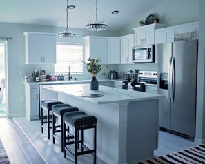 Uma cozinha moderna com ilha central, banquetas, eletrodomésticos de aço inoxidável e iluminação pendente.