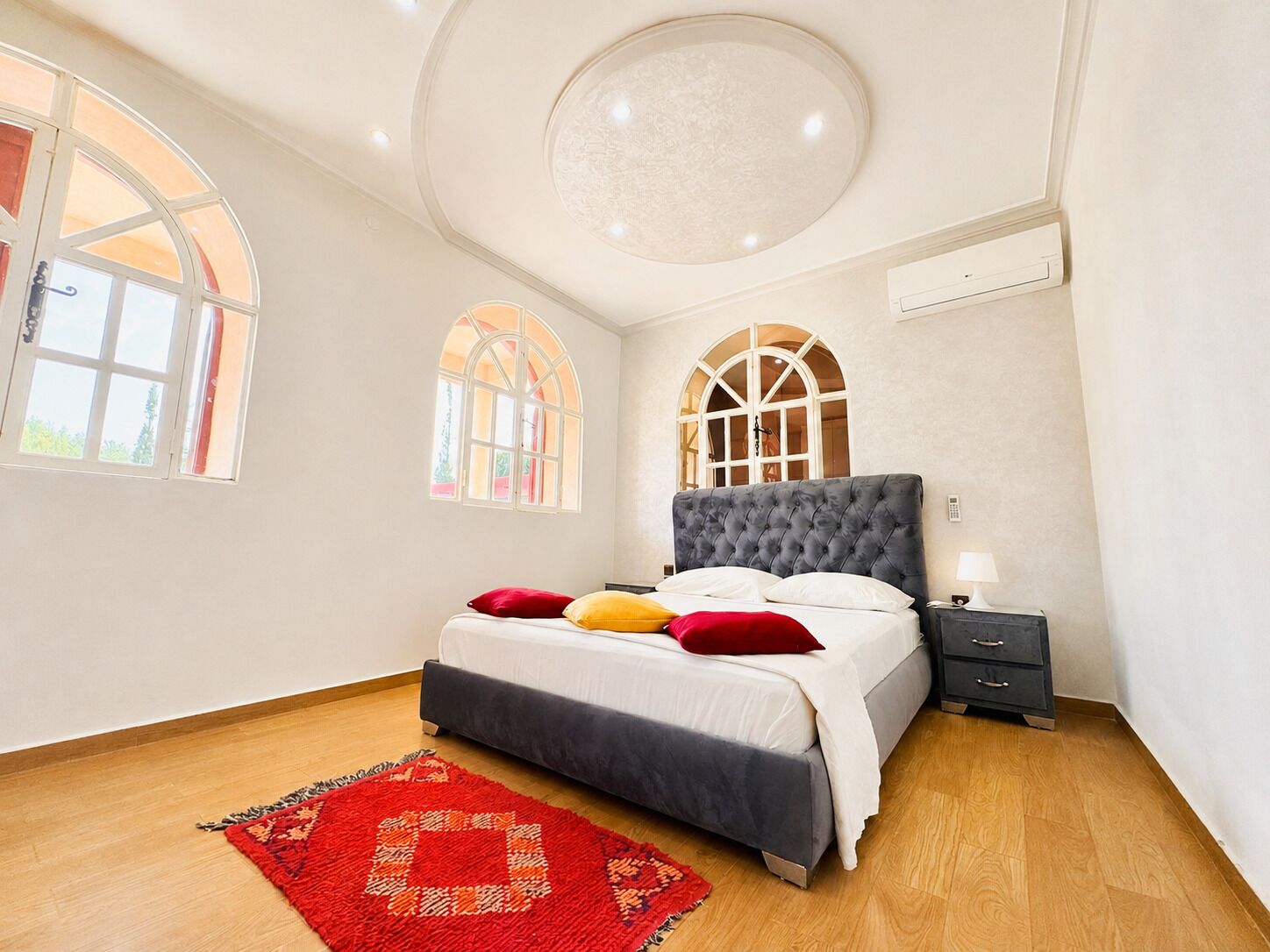 Une chambre à coucher avec un lit, une table de chevet, un tapis rouge et des fenêtres en arc de cercle.