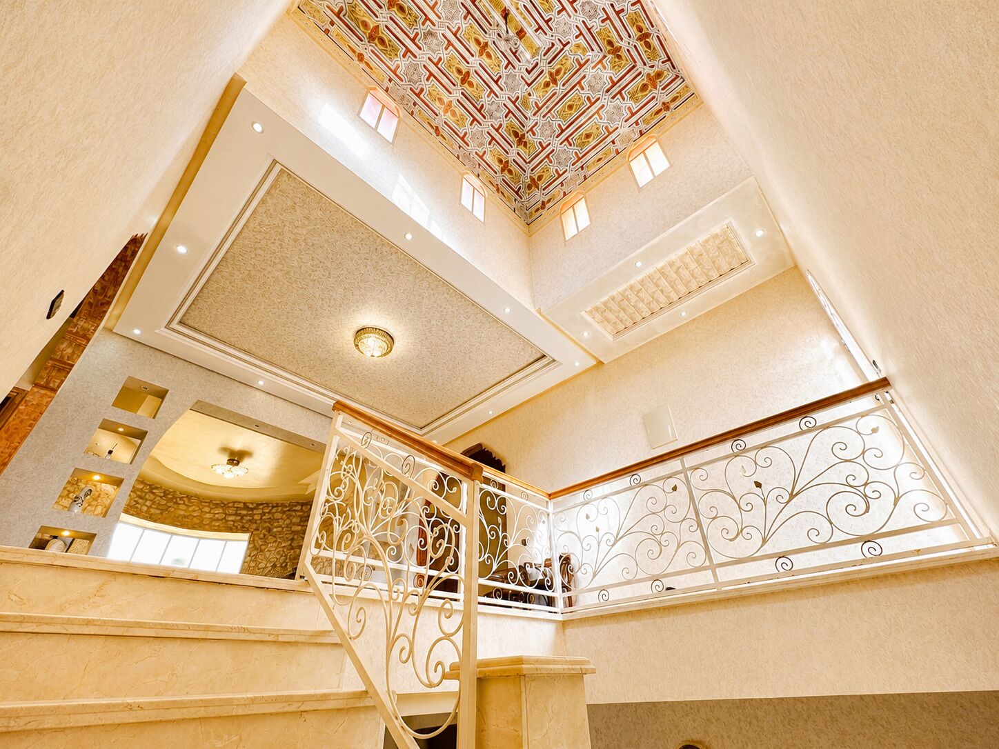 Un intérieur à plusieurs niveaux, agrémenté d’un plafond décoratif, d’un escalier avec des rampes ouvragées et d’un mur orné de motifs.