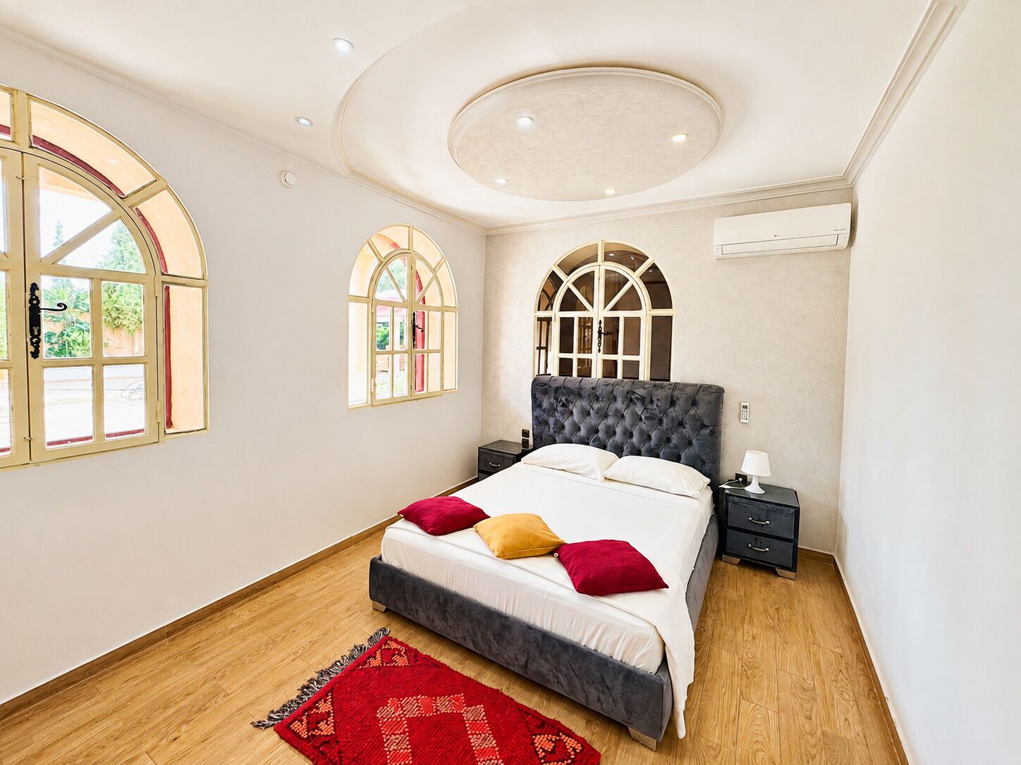 A bedroom with a large bed, two nightstands, a red rug, and a circular ceiling light.