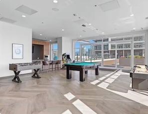 A modern indoor recreational area with a pool table, foosball table, and a bar area.