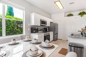 A modern kitchen with white cabinetry, stainless steel appliances, and a dining area with a table set for four. - 4BR Family Retreat with Private Pool (Davenport)