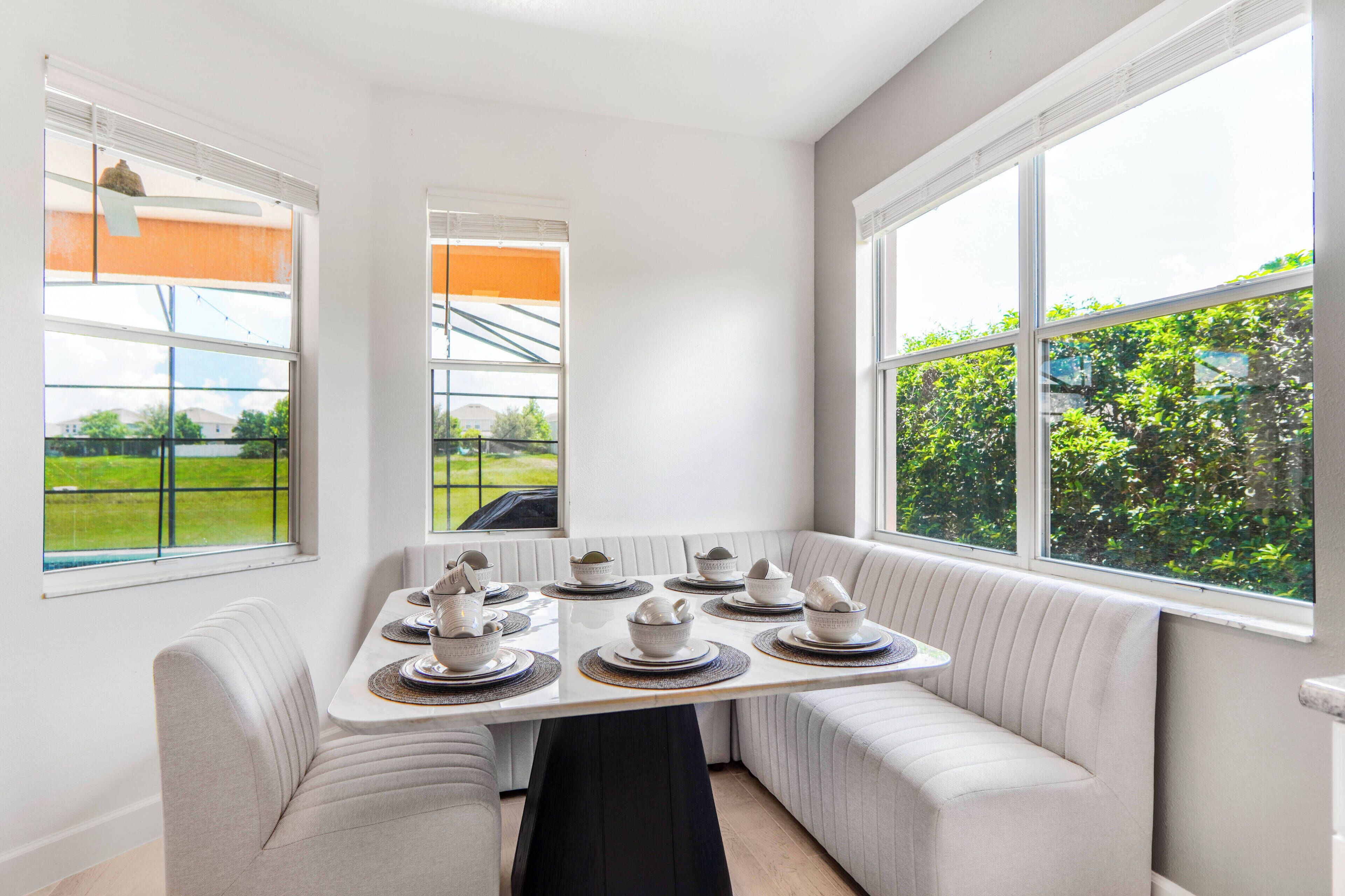 Un espace repas avec une table dressée pour quatre personnes, entouré de sièges confortables, de grandes fenêtres offrant une vue sur la verdure et un intérieur épuré et moderne.
