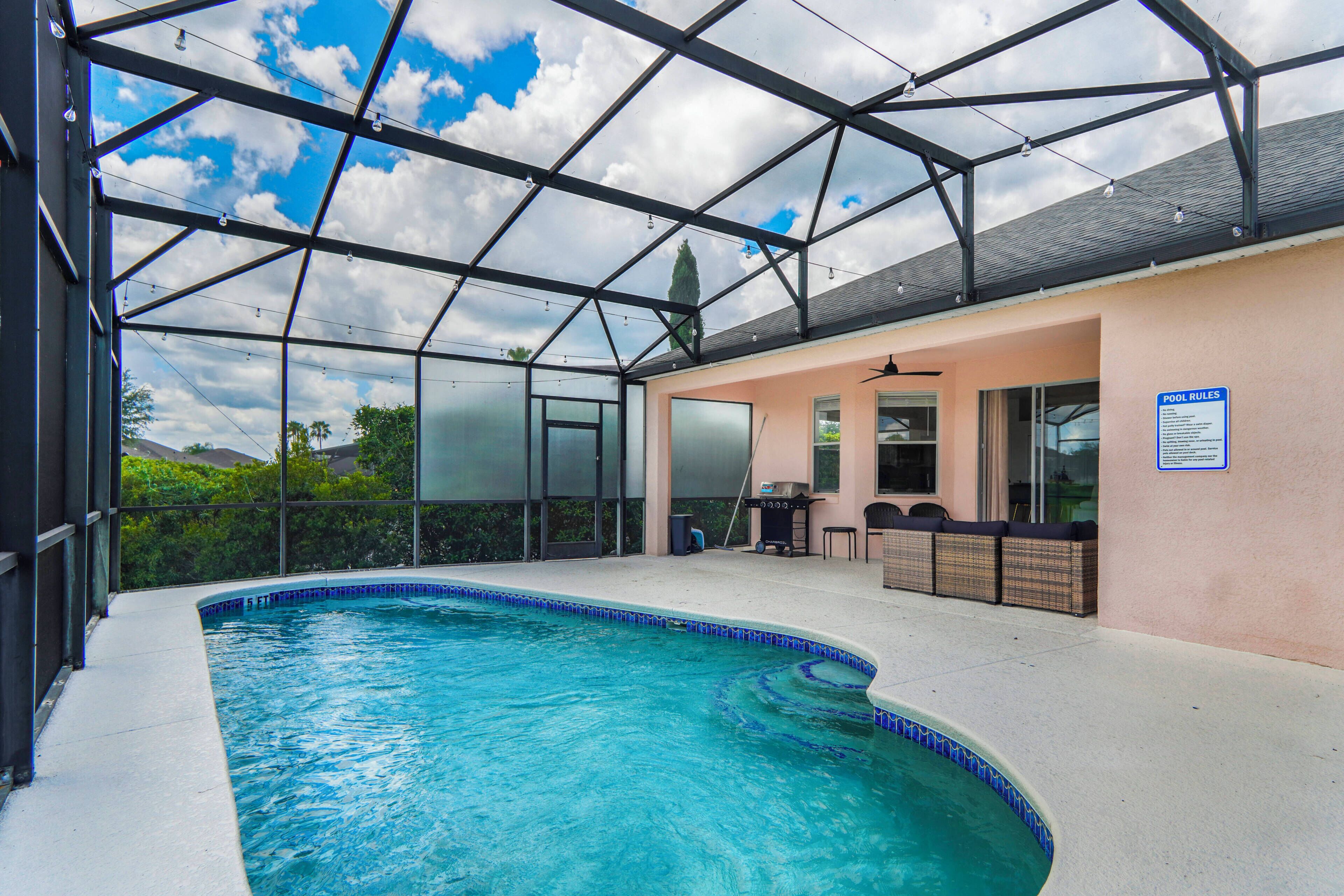 Una piscina interior con techo de cristal, zona de barbacoa y mobiliario junto a la piscina.