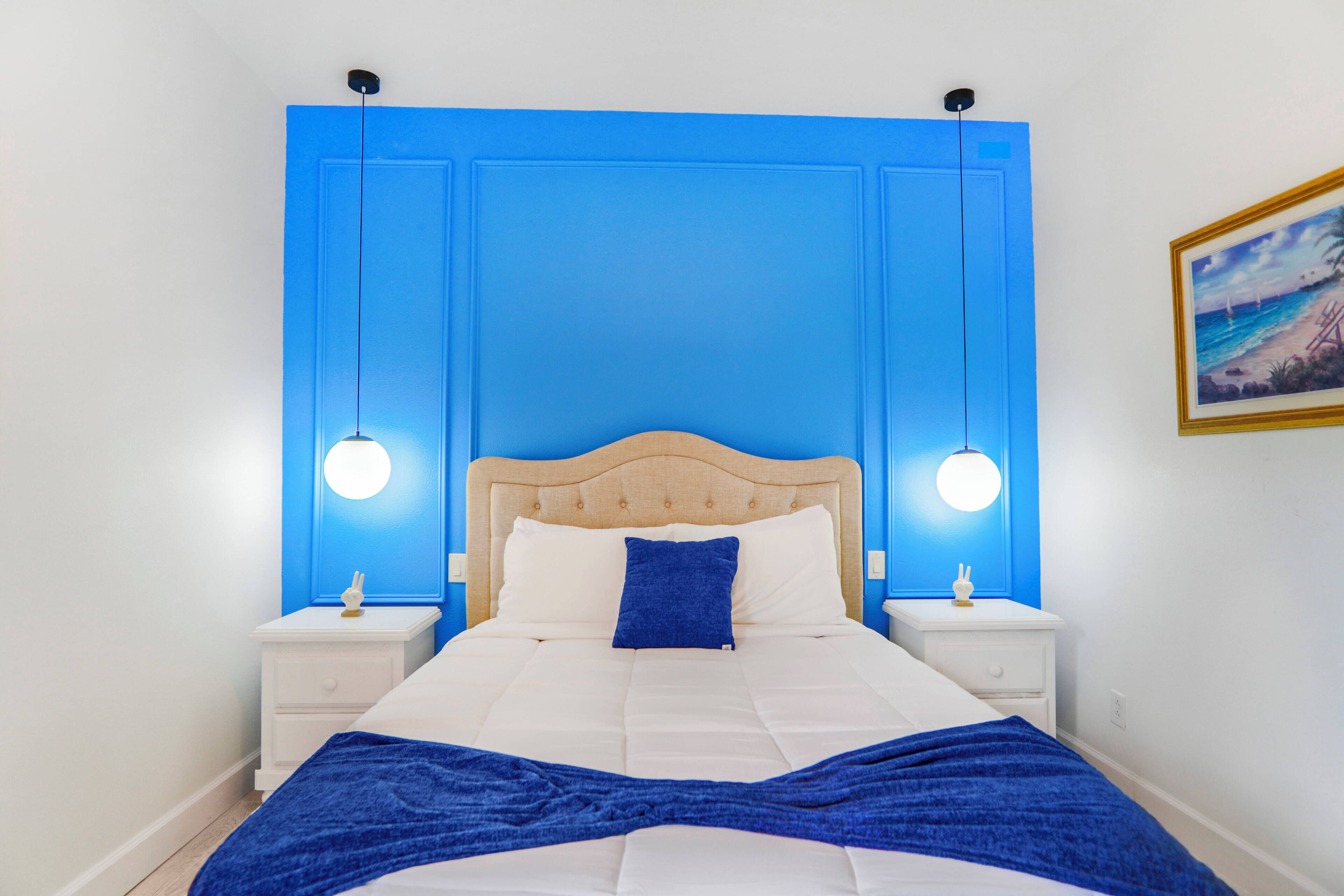 Ein Schlafzimmer mit einem Bett, zwei Nachttischen, einer blauen Wand und einem Bild an der Wand.