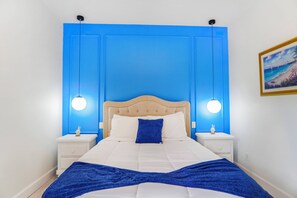 Une chambre à coucher avec un lit, deux tables de chevet, un mur bleu et un tableau accroché au mur.