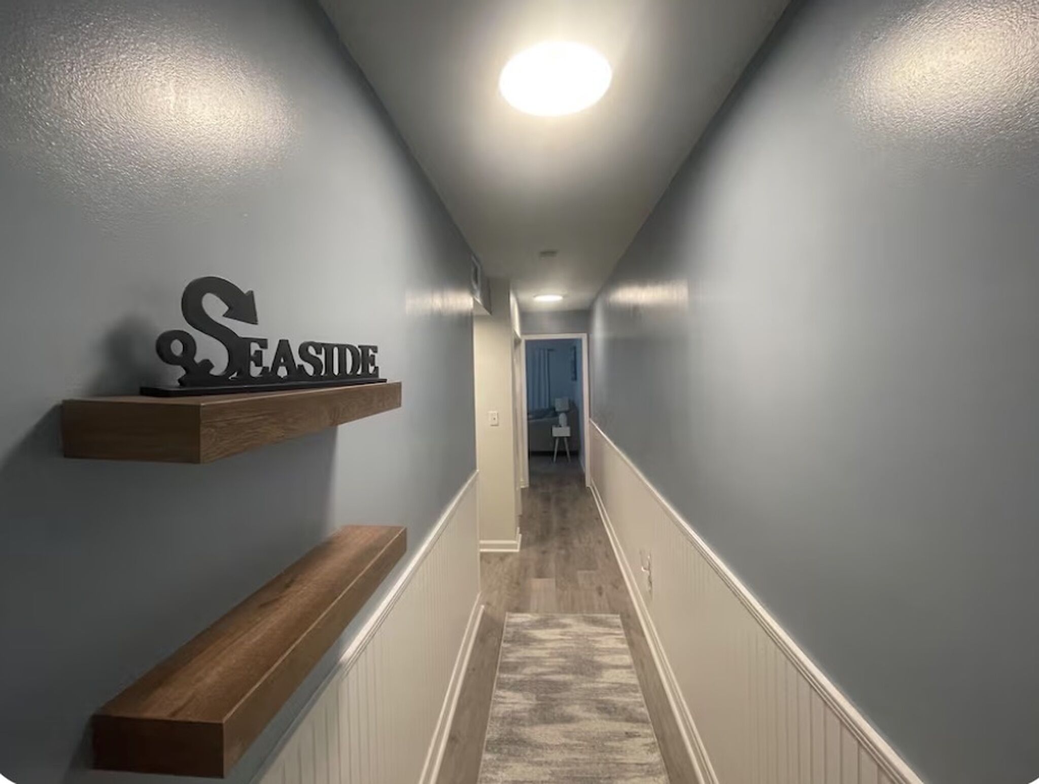 Un couloir avec un banc en bois, une enseigne fixée au mur et une porte au fond.