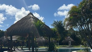 Una piscina con agua azul cristalina, rodeada de palmeras y estructuras con techo de paja.
