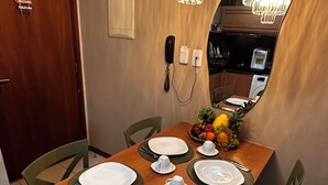 Comedor con mesa de madera dispuesta para cuatro personas, rodeada de sillas, una cesta de frutas y una araña.