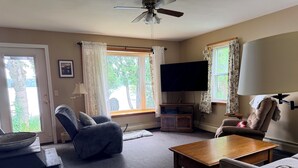 Ein Wohnzimmer mit Deckenventilator, einem an der Wand befestigten Flachbildfernseher, einem Holztisch, zwei Sofas und einer Fernsehbank.