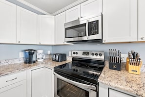 Una cocina moderna con armarios blancos, estufa de acero inoxidable, microondas, cafetera y bloque para cuchillos.