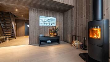 A modern living room with a wooden interior, a fireplace, a staircase, and a mounted artwork.