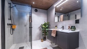 A modern bathroom with a glass shower enclosure, a sink with a towel, and a potted plant.
