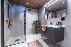 A modern bathroom with a glass shower enclosure, a sink with a towel, and a potted plant.